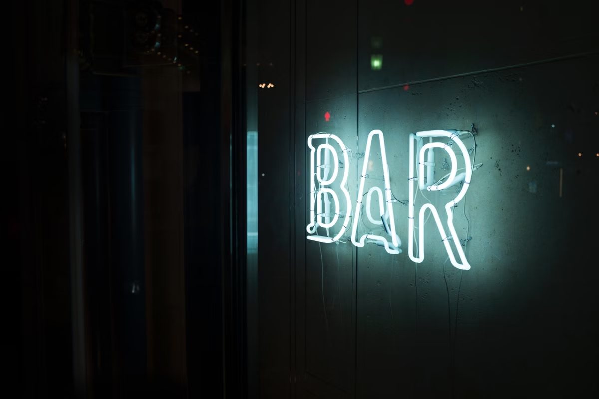 Verlicht neonbord van een bar tegen een donkere achtergrond